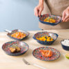 A gourmet culinary creation plated elegantly inside a bohemian mandala oval ceramic serving bowl with dual handles on a restaurant table.