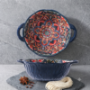 A hot cheese gratin freshly served in a bohemian mandala round ceramic baking dish on a bistro table.