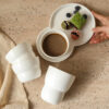 stackable-handless-ceramic-cups A stack of white glossy handless ceramic cups with a distinctive wavy textured design for space-saving storage.