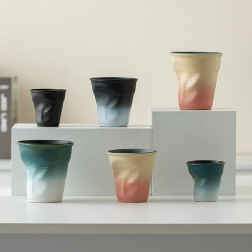 wholesale-creative-crumpled-ceramic-cups A wholesale display of creative crumpled ceramic cups in various gradient matte colors and sizes for cafe supply.