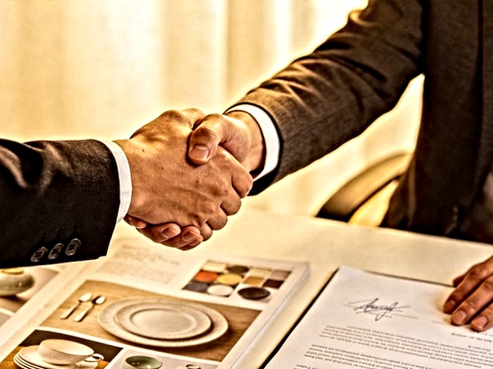 business handshake over signed ceramic tableware purchase contract with product catalog on modern office desk representing B2B partnership