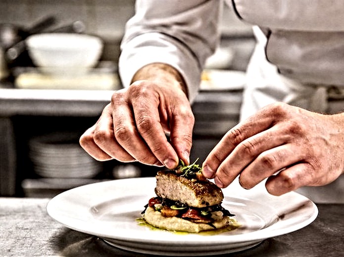 chef plating dish on white ceramic plate in commercial kitchen for restaurant service
