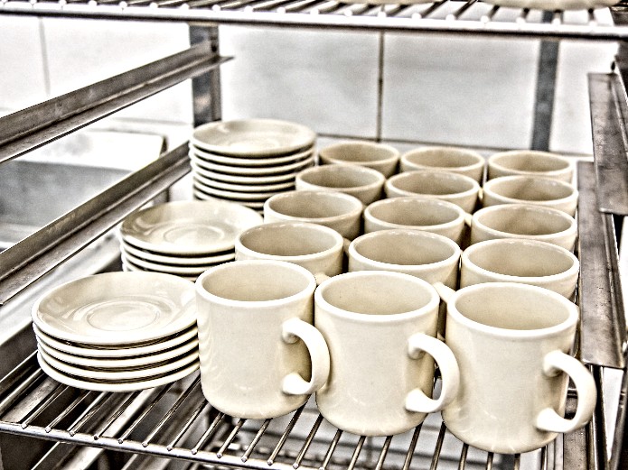 durable ceramic mugs and bar plates stacked in a commercial kitchen dish rack for hospitality use