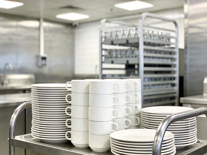 stacked white ceramic plates and cups on stainless steel cart in airport lounge prep kitchen