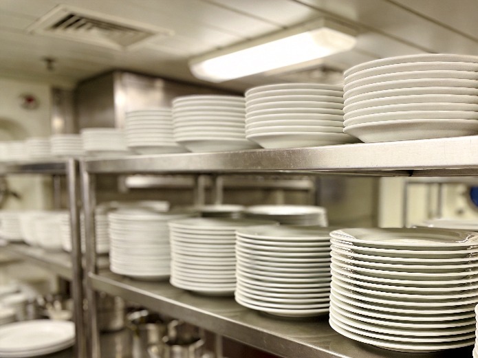 cruise ship galley with stacks of durable porcelain plates organized on stainless steel shelving