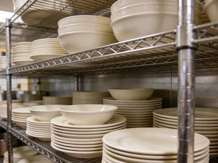 stacked ceramic plates and bowls on stainless steel shelving in resort kitchen storage